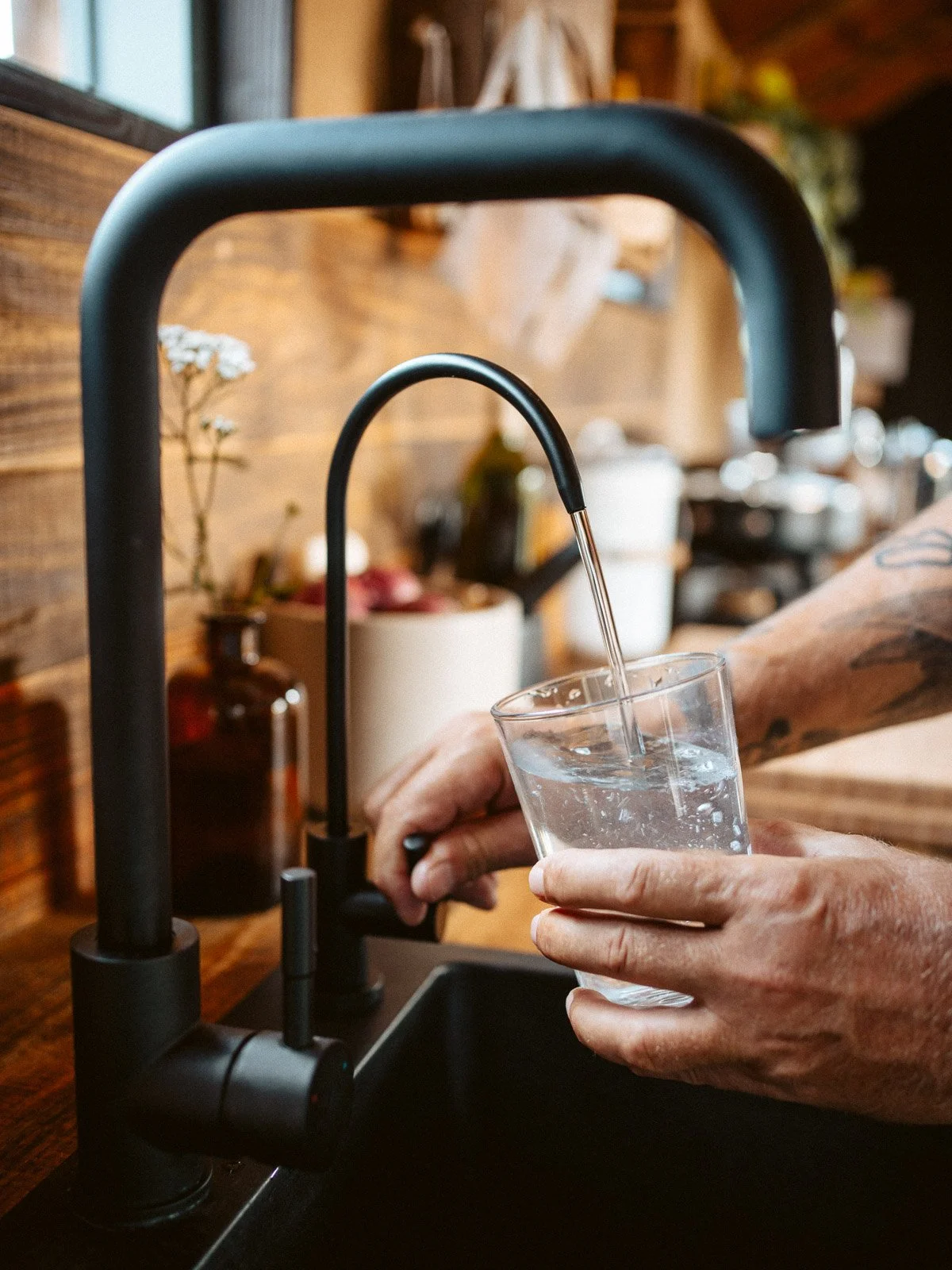 Hand mit Tattoo füllt Wasser in ein Glas unter einem Wasserhahn in einer Küchenspüle.