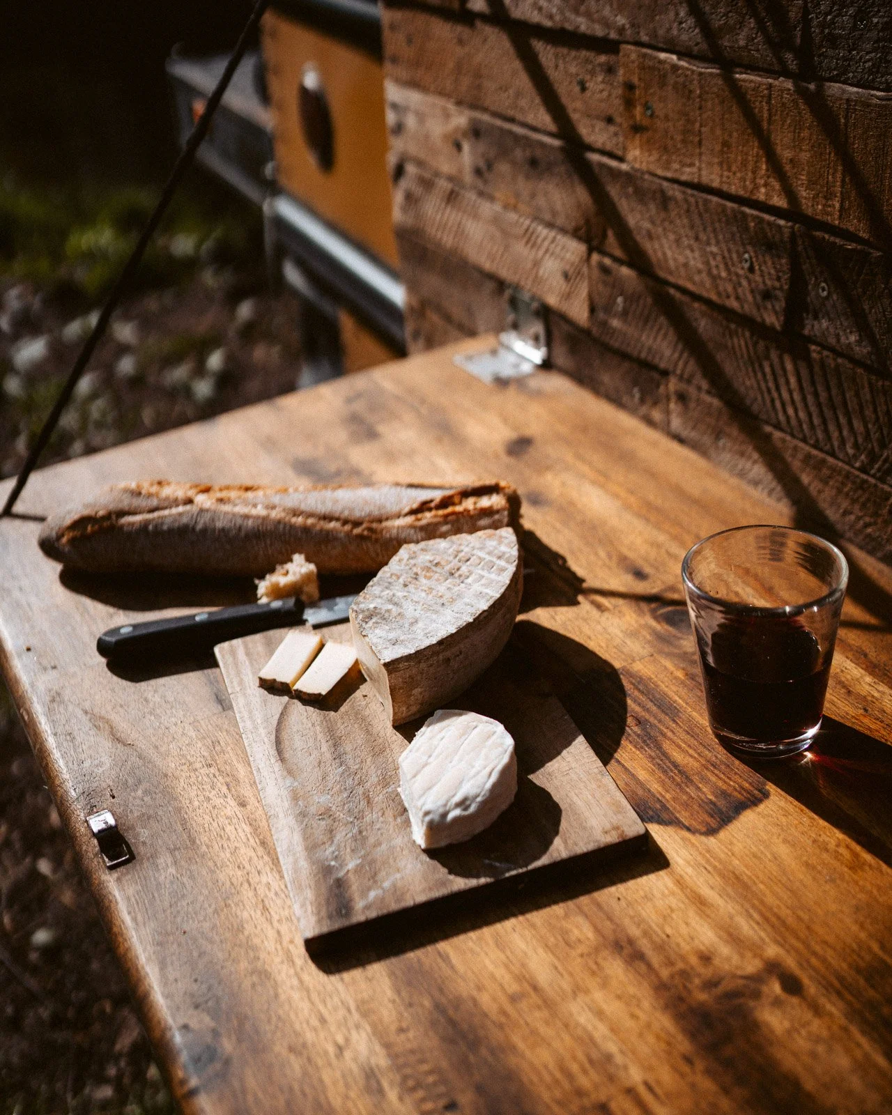 Käseplatten mit verschiedenen Käsearten, Baguette, ein Messer, ein Glas Rotwein auf einem Holztisch.