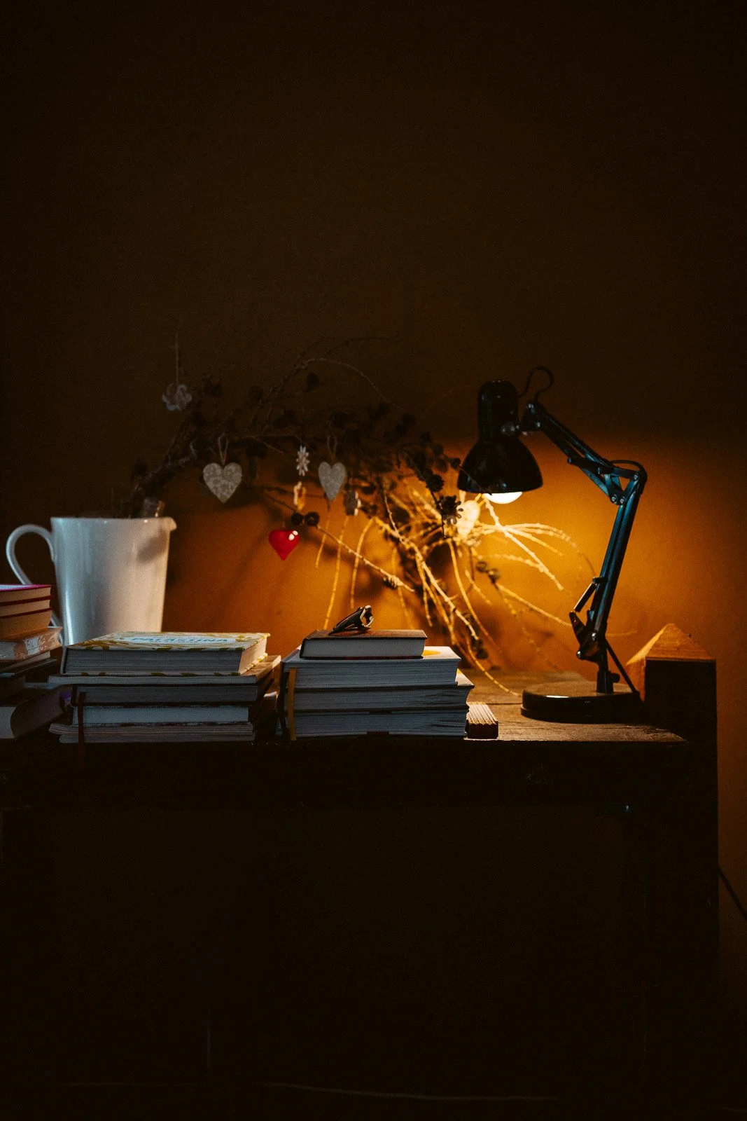 Schreibtisch mit Büchern, Schreibtischlampe, Kaffeetasse, dekorativem Zweig mit Herz- und Sternanhängern