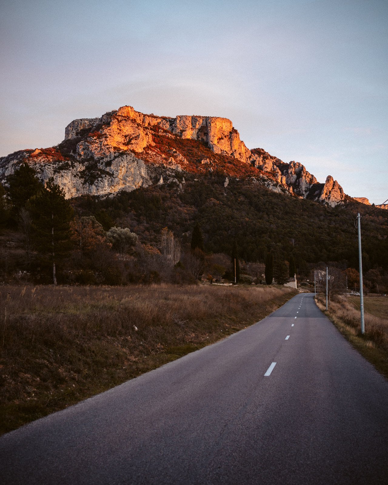 eine leere Straße führt zu einem Berg im Sonnenuntergang, mit Bäumen entlang der Seite