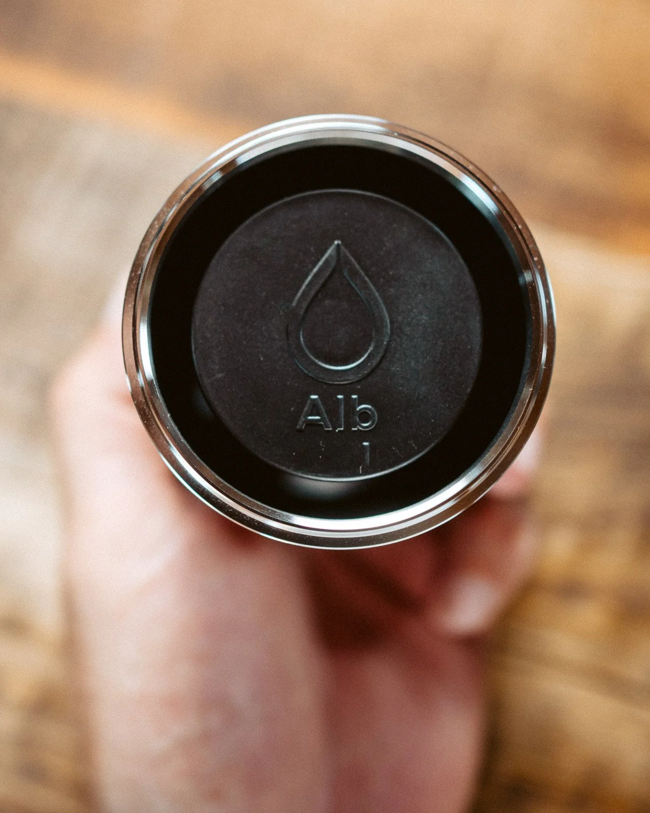 Vogelperspektive auf eine schwarze Dose mit einer Wasserraute-Form und der Beschriftung 'A15' auf der Oberseite, gehalten von einer Hand.