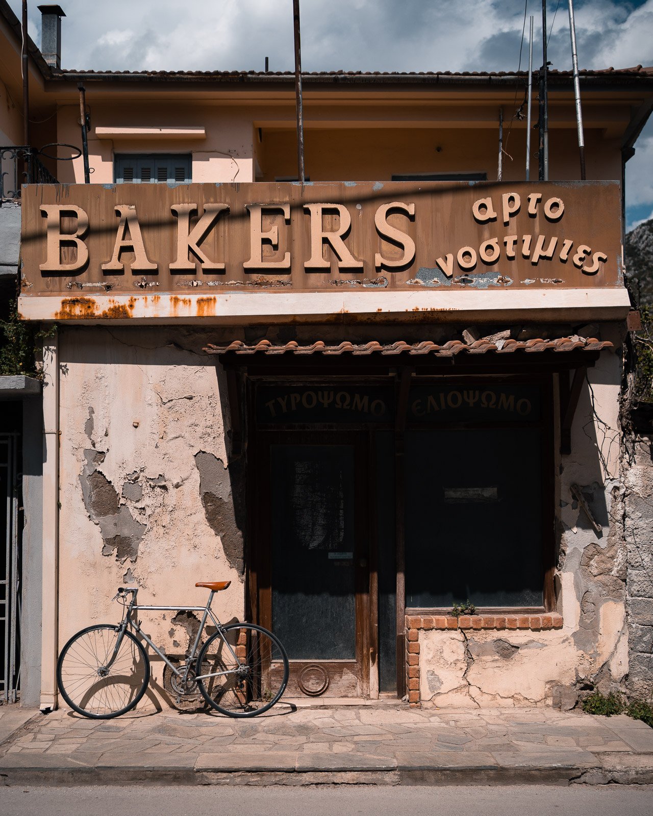 Verwittertes Geschäft mit einem Schild 'BAKERS' und einem Fahrrad vor der Tür.