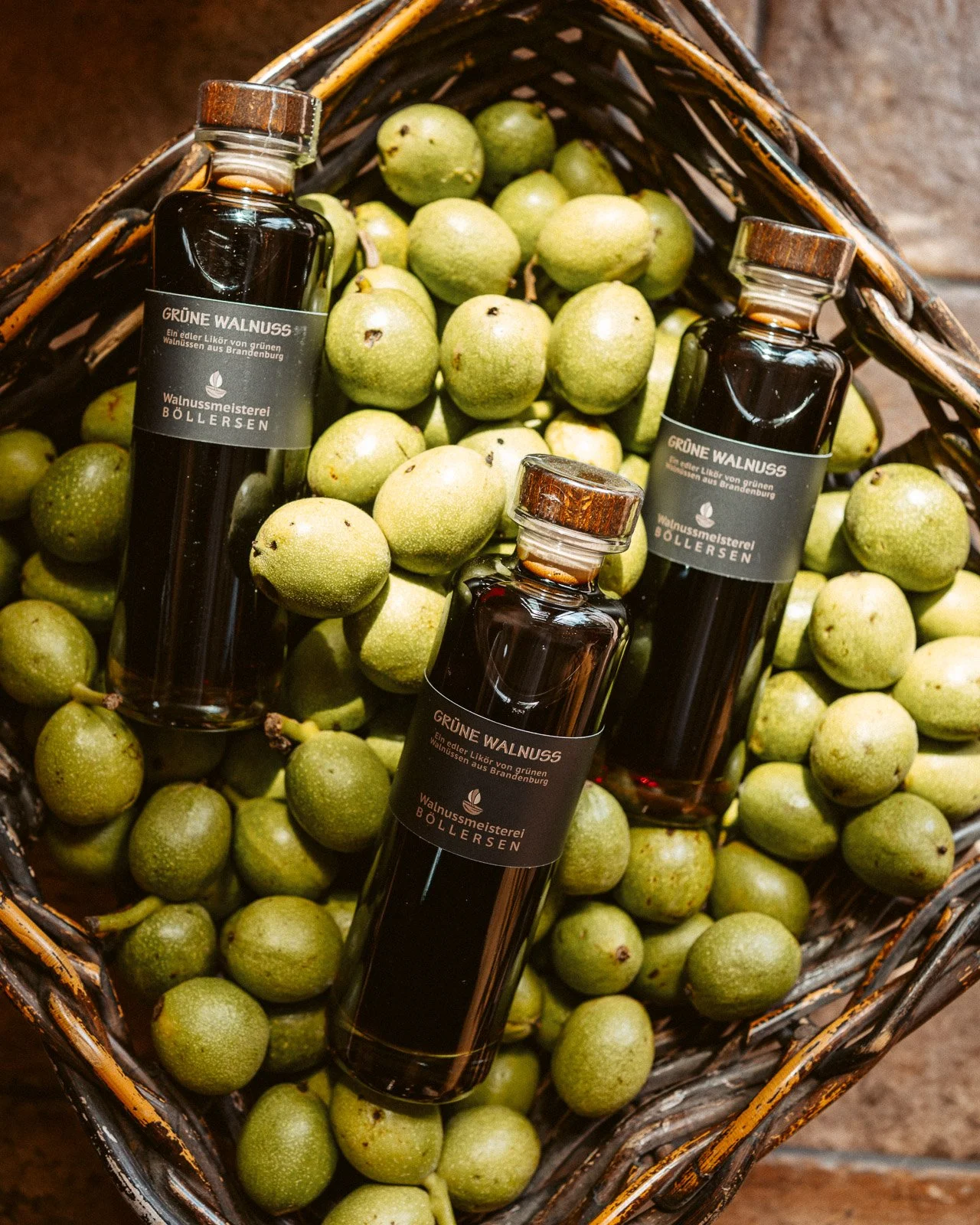 Ein Korb voller grüne Walnüsse mit drei Flaschen Grüne Walnuss Likör.