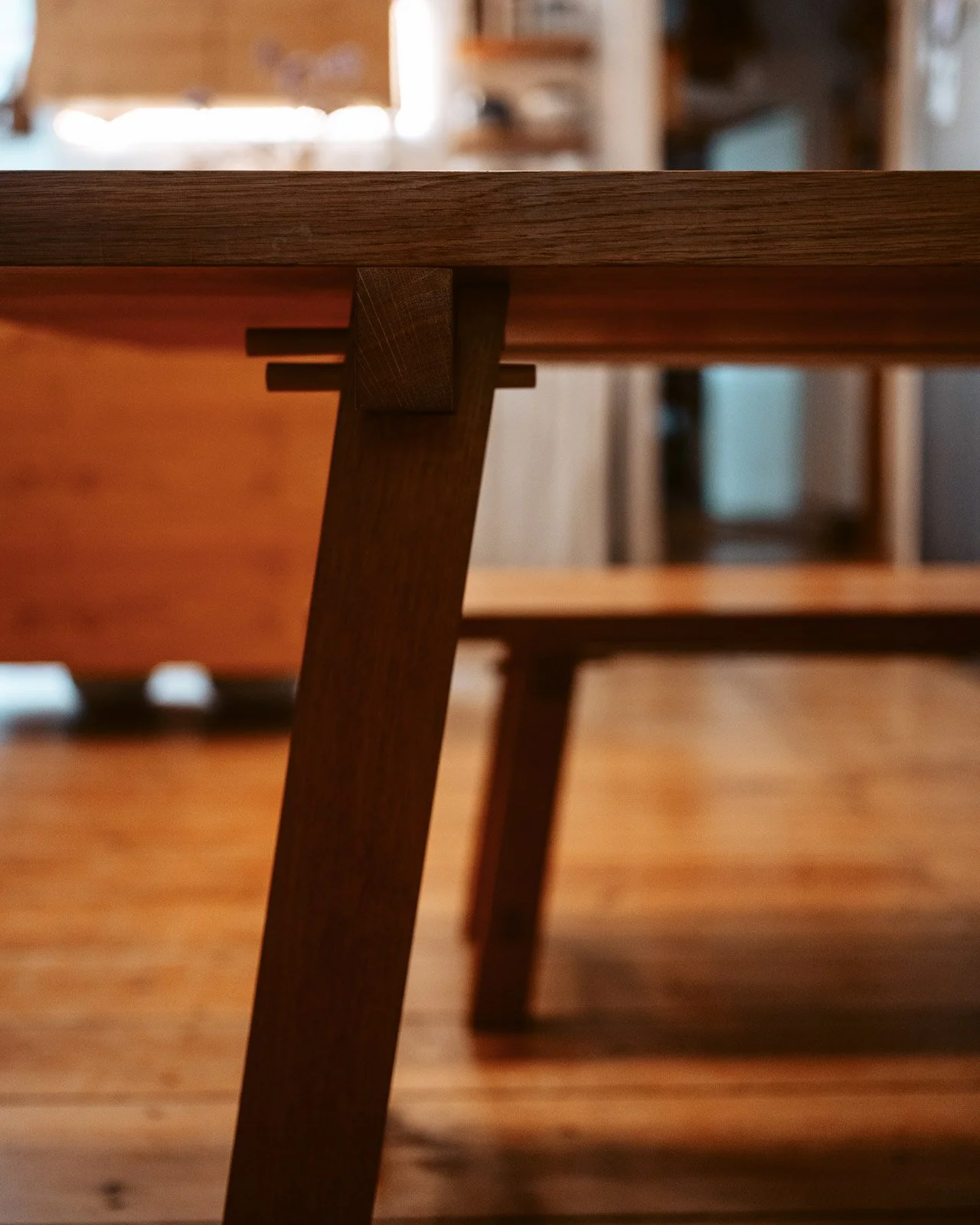 Nahaufnahme eines Holztisches und Stuhls, im Hintergrund einige Möbel und ein Fenster in einem Raum.