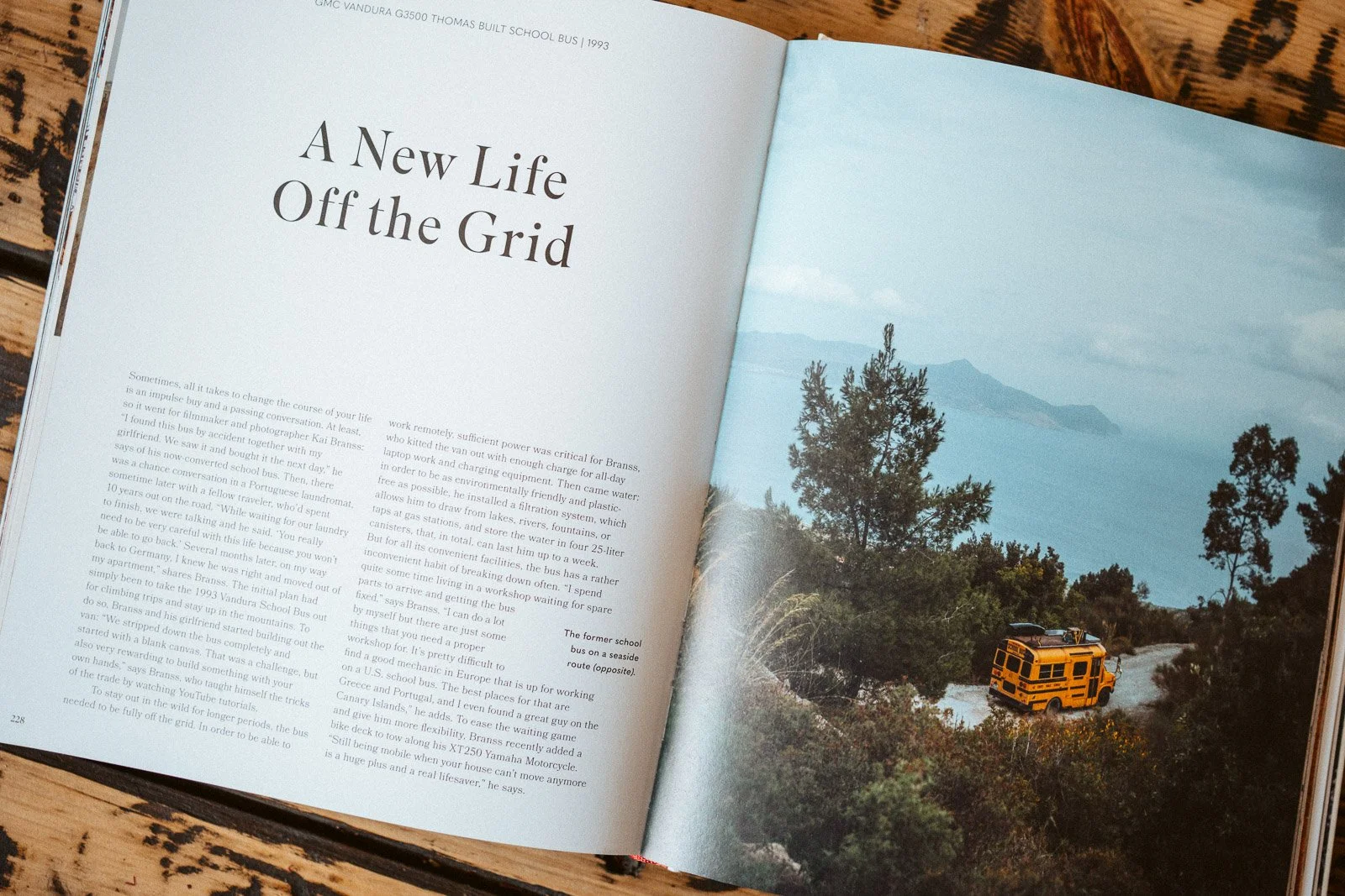 Offene Zeitschrift mit dem Titel 'A New Life Off the Grid'. Auf der rechten Seite ein Bild eines Busses in der Natur mit Bäumen, Wasser und Bergen im Hintergrund.