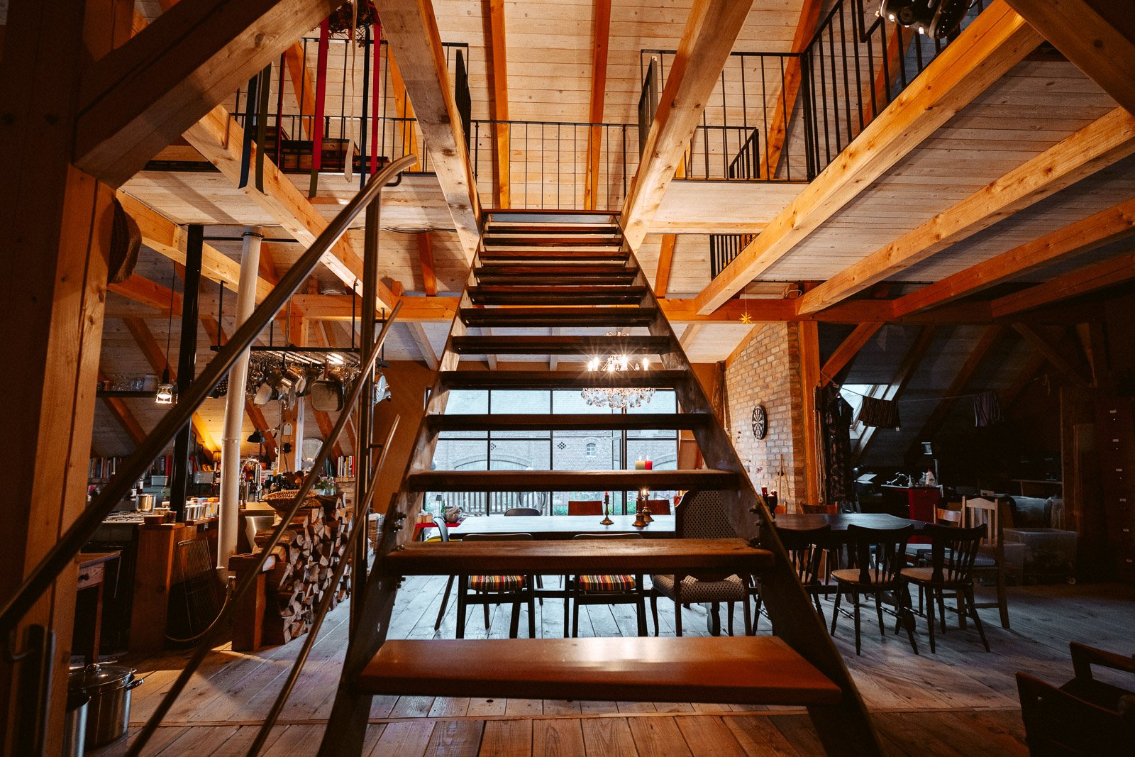 Innenansicht eines mehrstöckigen Hauses mit Holztreppe, Ess- und Wohnbereich, Holzboden und sichtbare Balken im Deckenbereich.