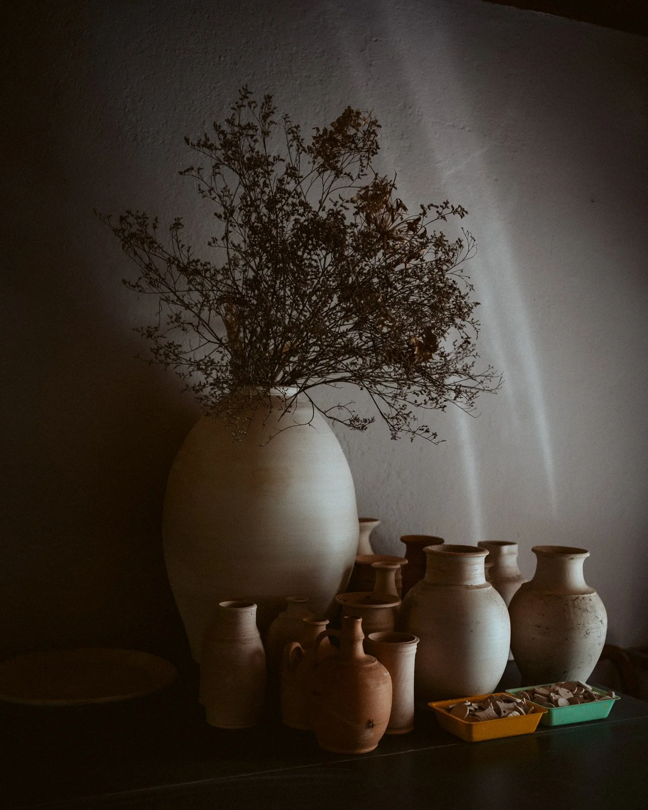 Bunte Keramikvasen und Trockenblumen auf einem Tisch, mit Schatten an die Wand geworfen.