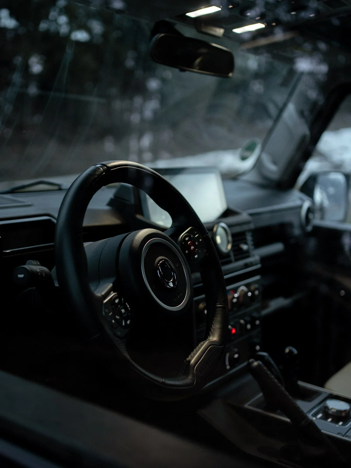 Innensicht eines Autos mit schwarzem Lenkrad, Armaturenbrett und Schaltknüppel bei Dämmerung, dunkle Atmosphäre.