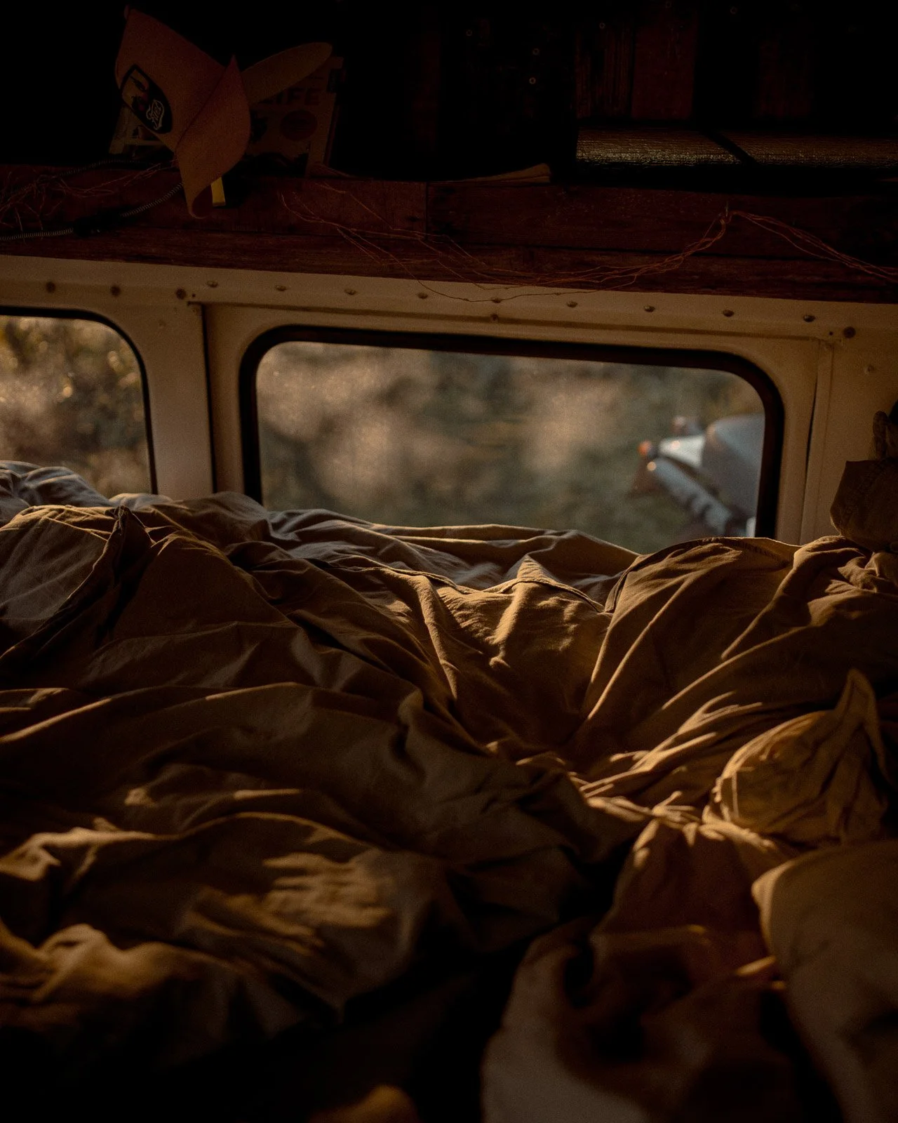 Bett im Inneren eines Versandswagens, Blick durch das Fenster auf eine Straße bei Sonnenuntergang.