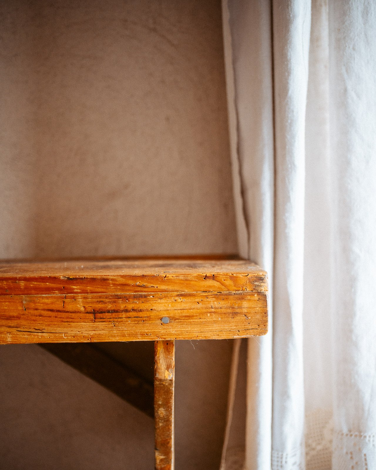 Ein Ausschnitt eines leeren Holzregals neben einer weißen Gardine