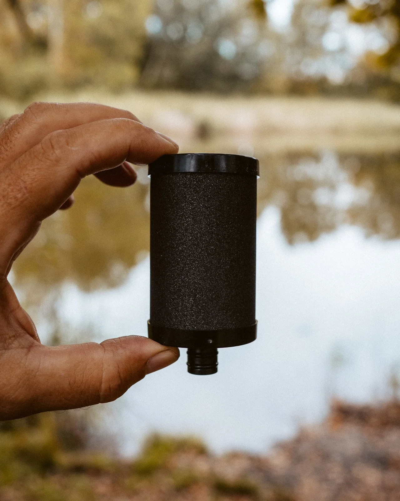 Person hält einen schwarzen Luftreiniger mit Wasser im Hintergrund.