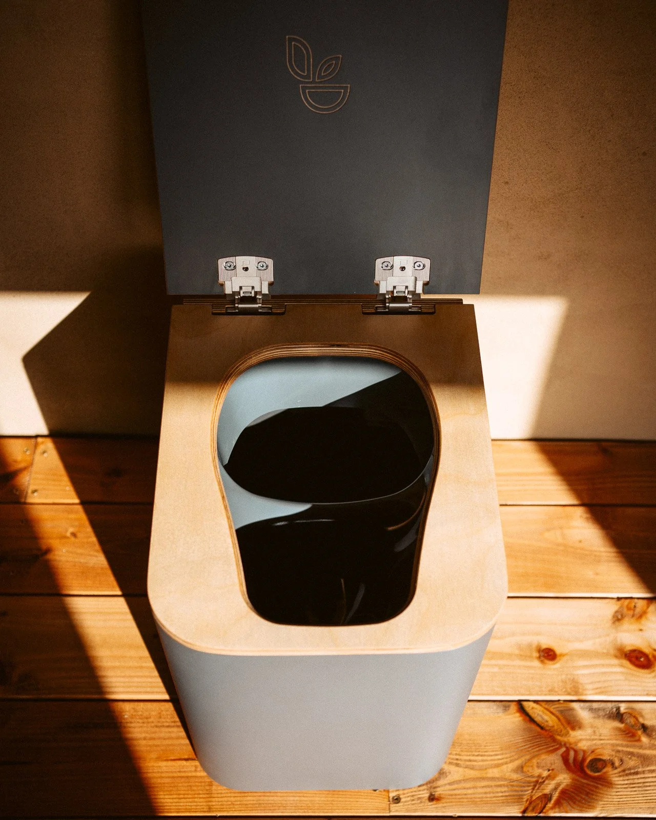 Ein Holzwc mit einem Deckel, der eine schwarze Innenschüssel hat, steht auf einem Holzboden.