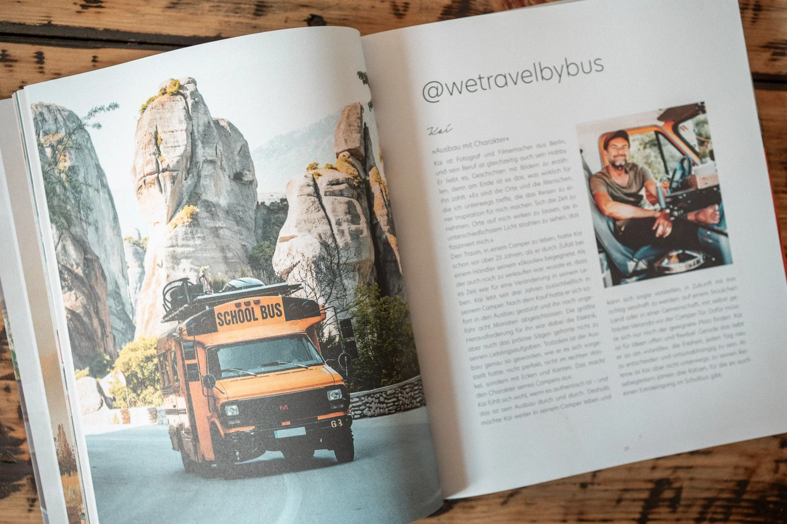 Offener Reiseführer mit einem Foto eines orangefarbenen Schulbusses unter Felsformationen, und einem Bild eines Mannes im Fahrerhaus, sowie ein Instagram-Handle '@wetravelbybus' und deutscher Text auf der rechten Seite.