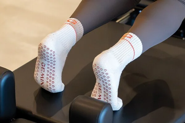 Woman wearing grip socks reaching forward during an advanced reformer Pilates class in Buderim