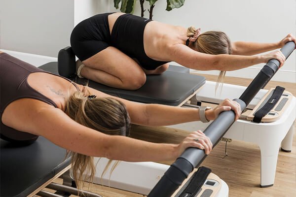 Women reaching forward on a reformer Pilates machine inside a Pilates studio in Bli Bli