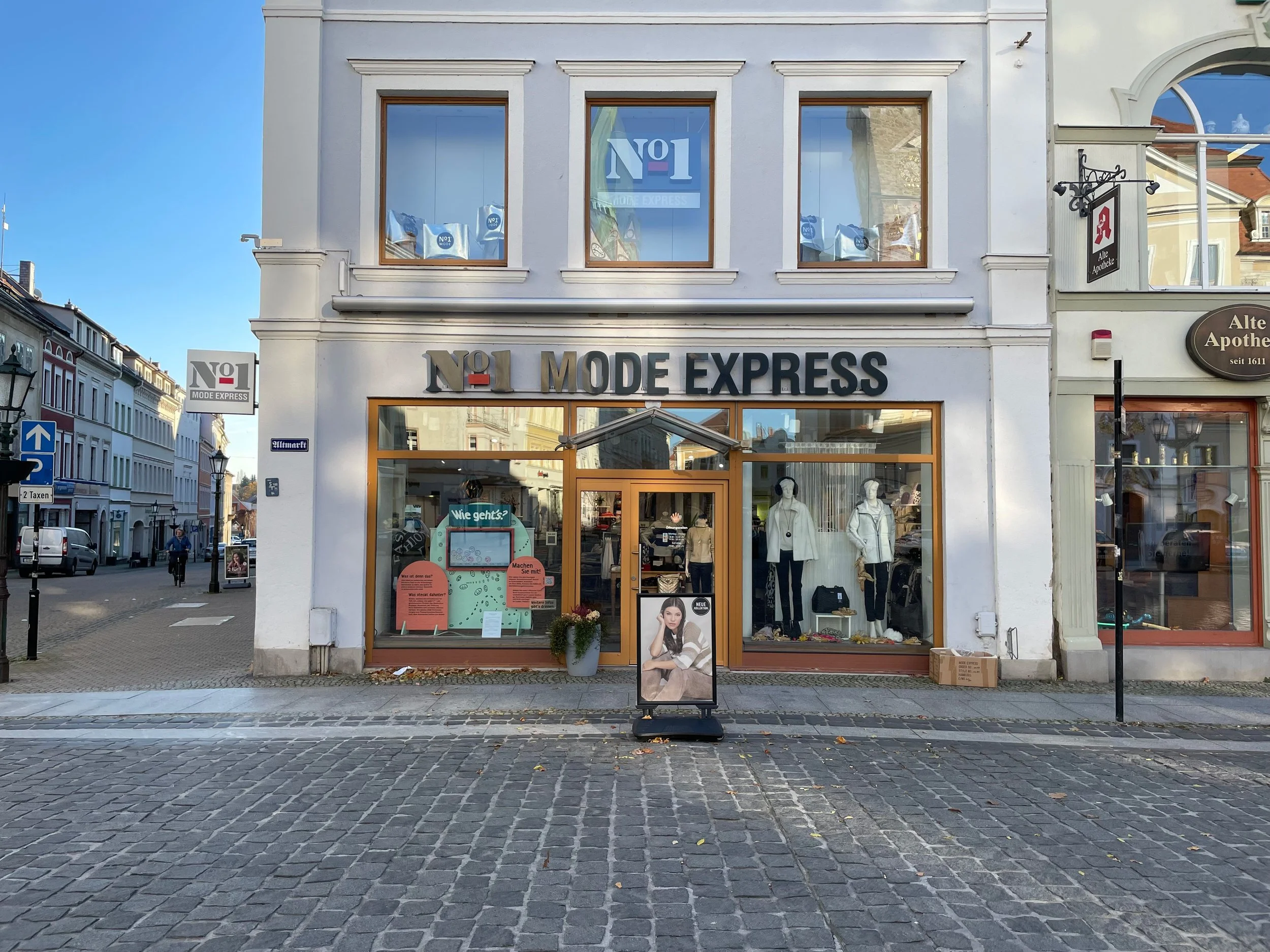 Schaufenster mit interaktivem Stimmungsbarometer und zwei orangefarbenen Informationstafeln mit Texten zu einem Projekt namens »Löbau, wie geht's?«