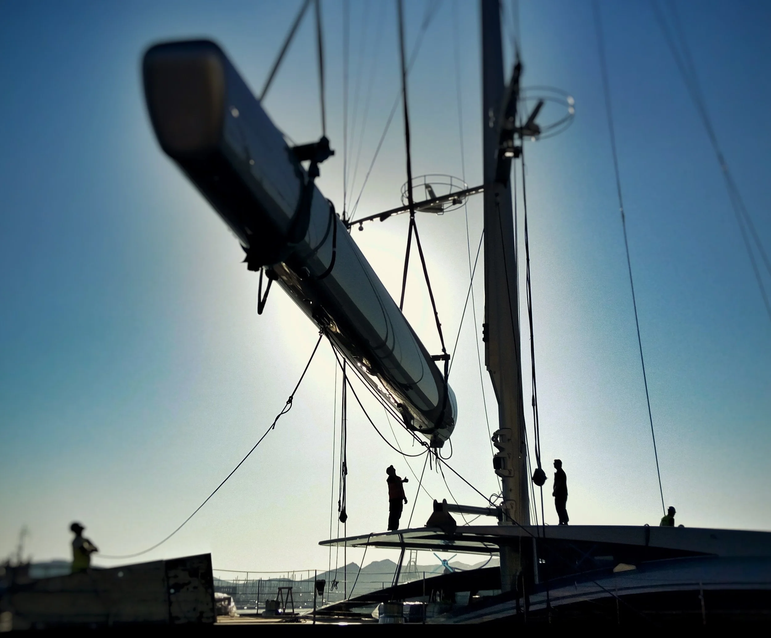 Silhouettes of people on a sailboat against bright sky, with the boat's mast and rigging in view.