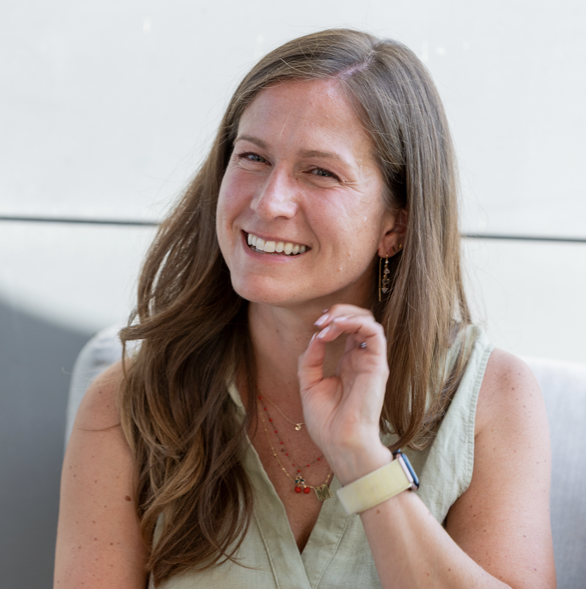 Woman with light brown hair smiling and waving her hand