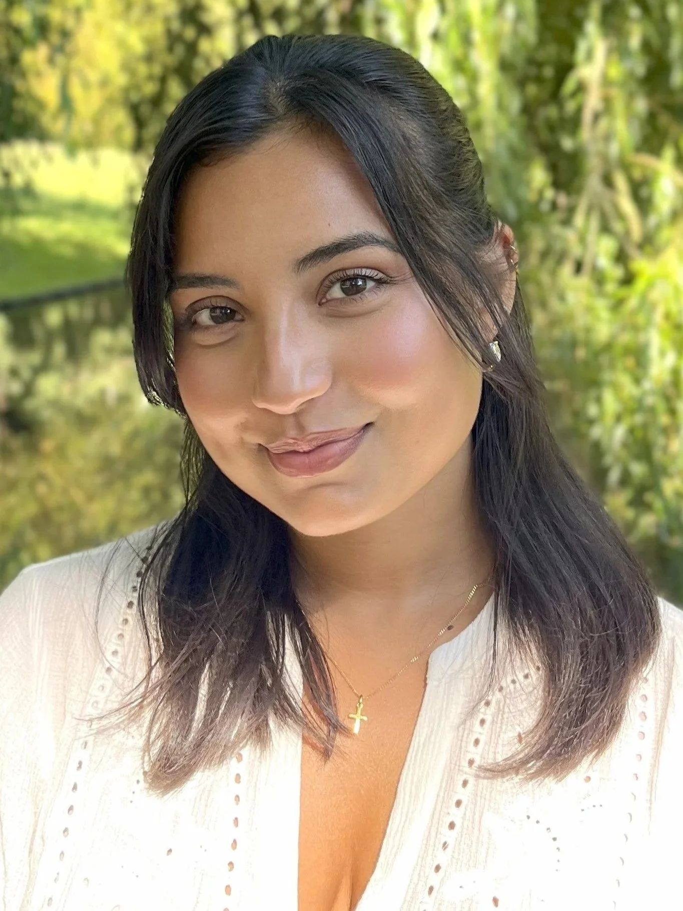 Young woman with dark hair smiling with a backdrop of green leaves