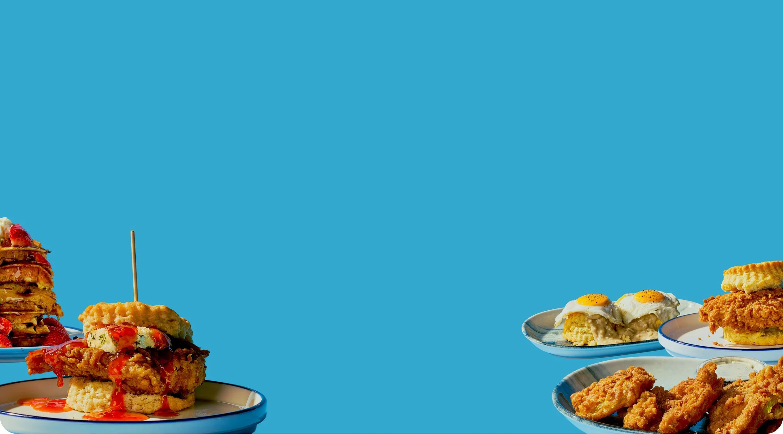 Various plates of fried chicken, biscuits with eggs, and dessert items on a blue background.