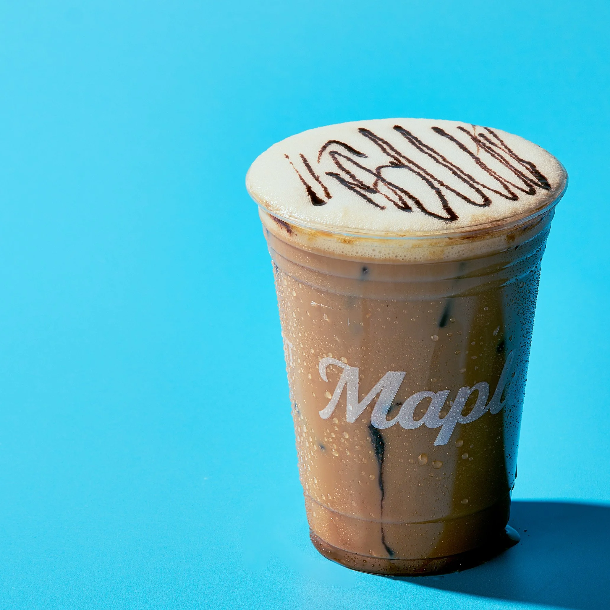 Close-up of a martini glass with frosted rim, filled with a creamy beverage, garnished with a drizzle of chocolate syrup on top, against a bright blue background.