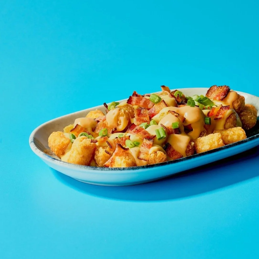 A bowl of macaroni and cheese topped with bacon bits and cheese sauce on a blue background.