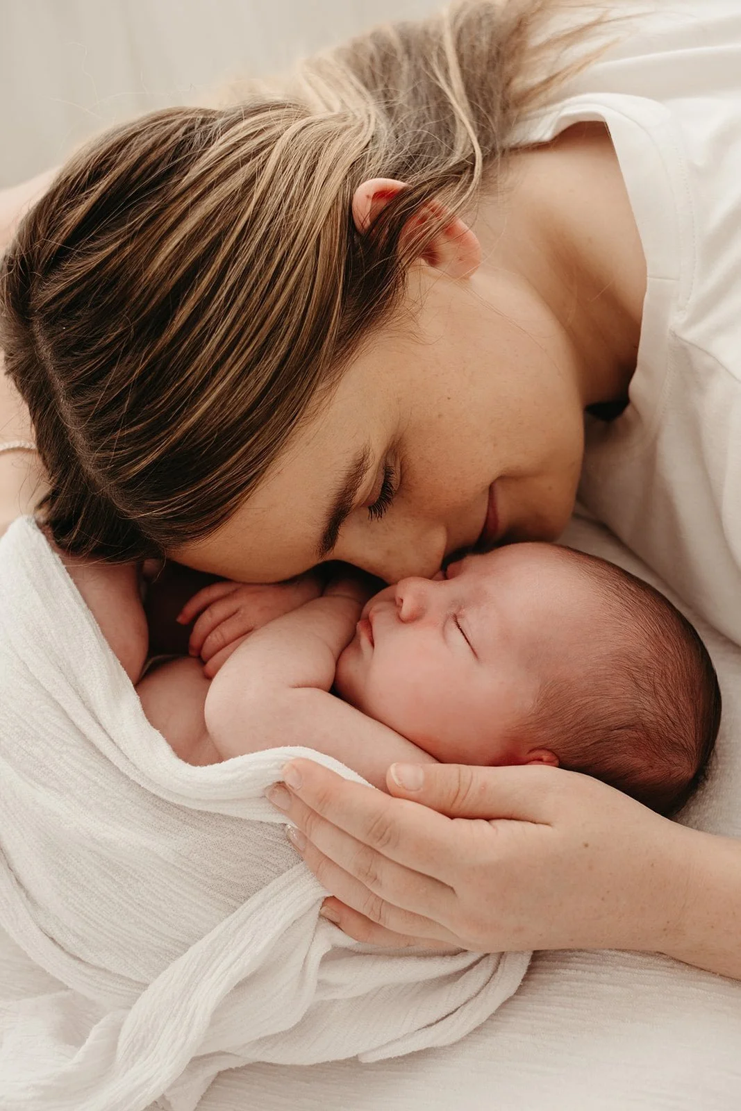 Et nyfødt baby ligger tett inntil en voksen kvinne som er sannsynligvis mor, begge med øynene lukket, i en kjærlig og fredelig gest.