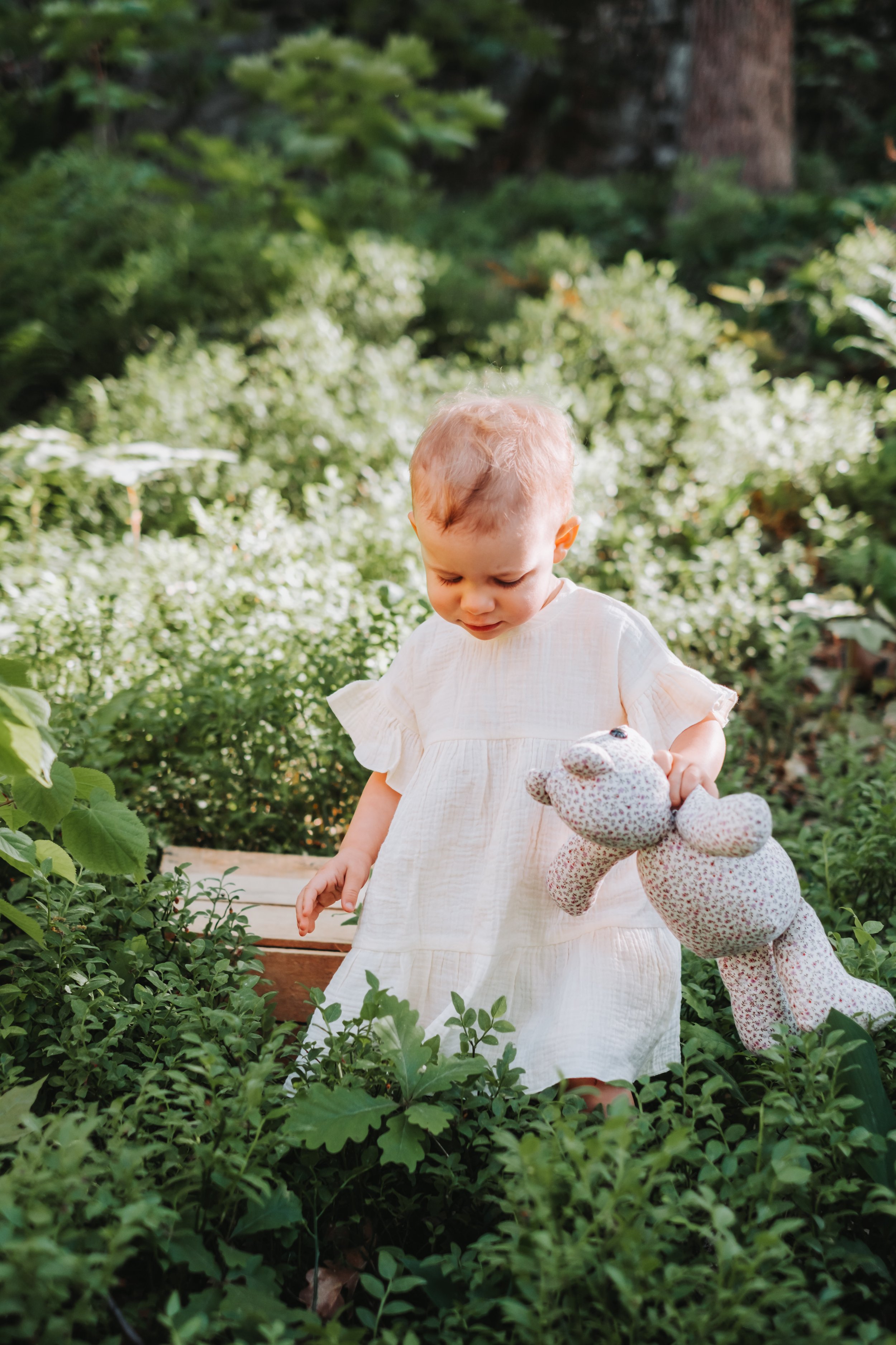 Toddler holding a stuffed animal in a garden