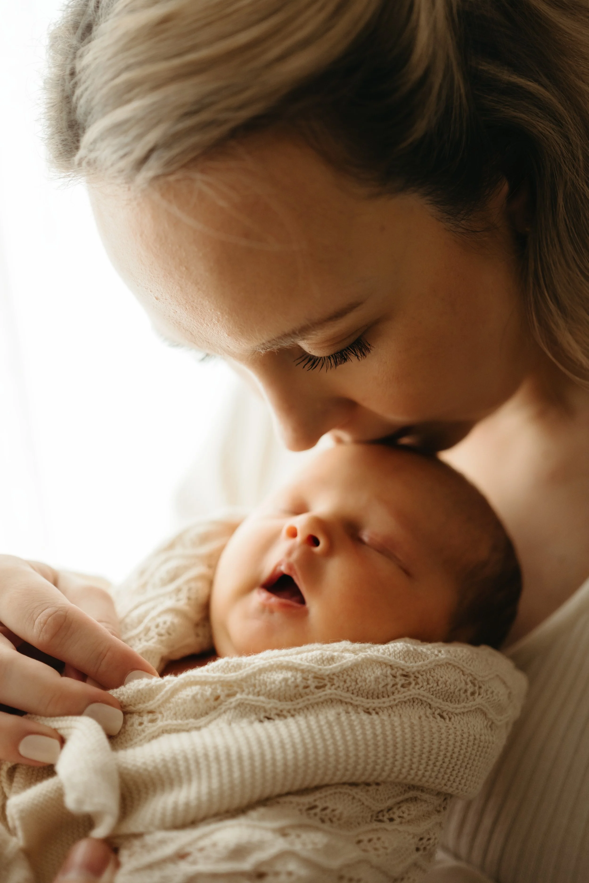 En kvinne holder en sovende baby nært, kysser pannen.