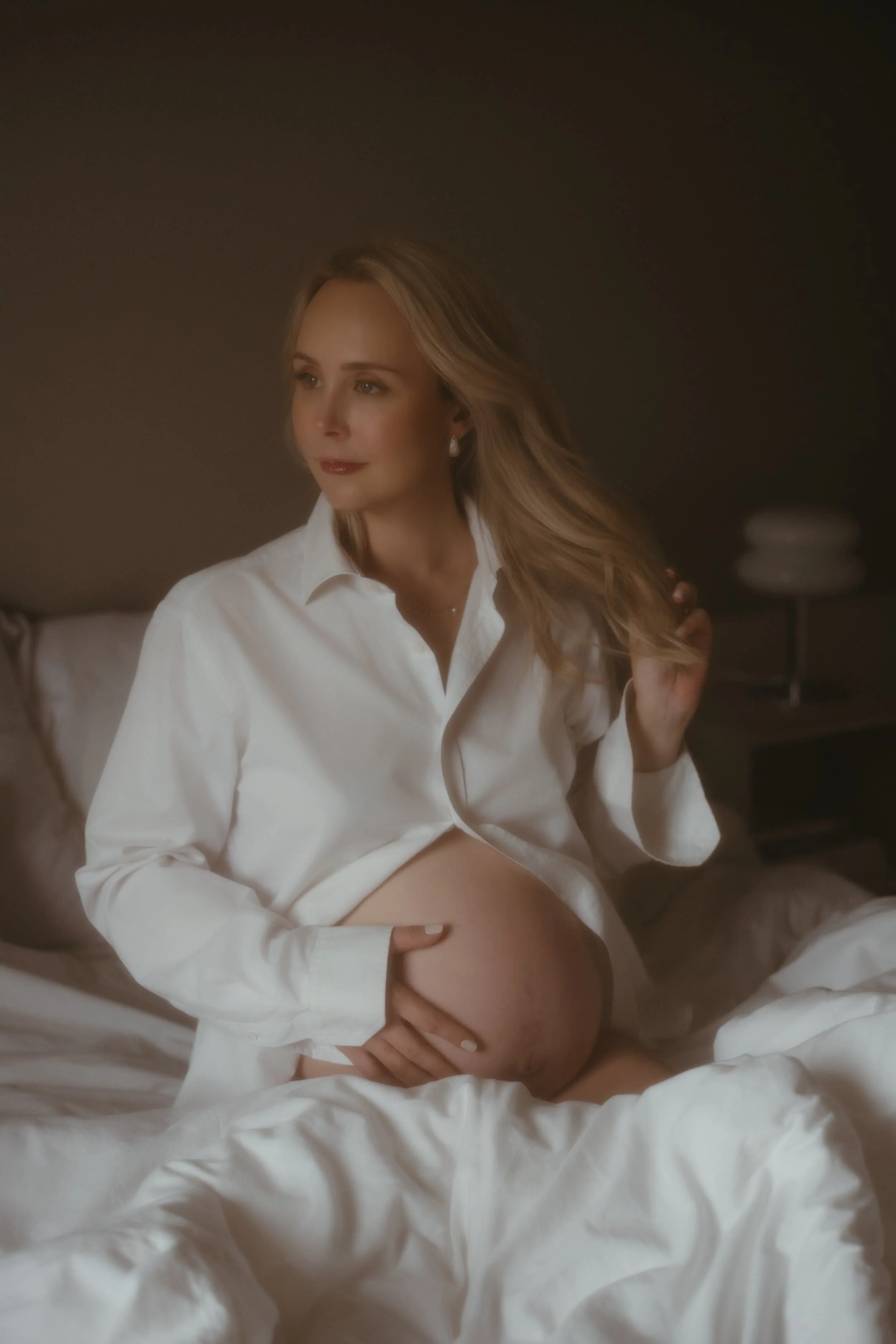 Et bilde av en gravid kvinne i en seng, iført en hvit skjorte, som forsiktig holder magen sin.