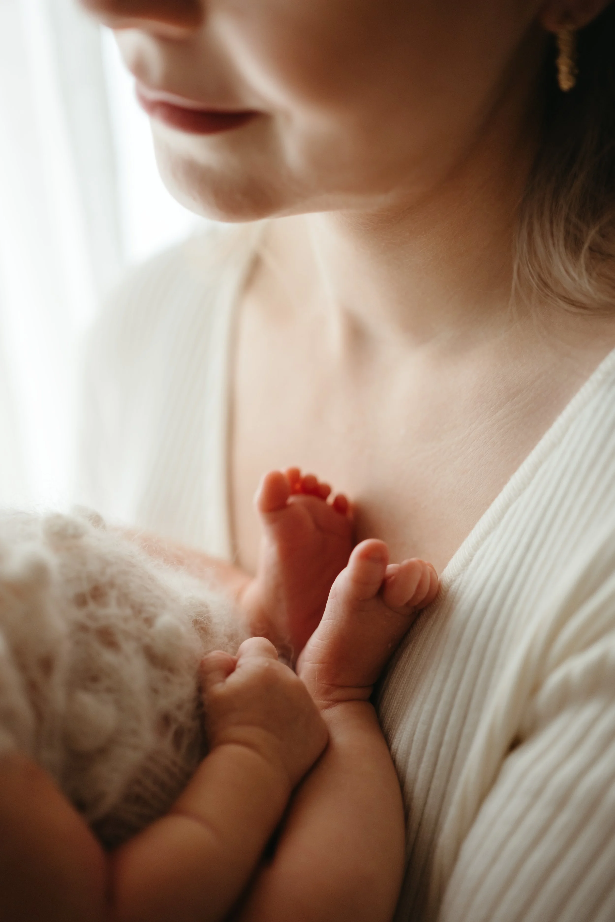 Nærbilde av en kvinne som holder en baby mot brystet sitt, med fokus på babyens små hender og kvinnens ansikt fra siden.