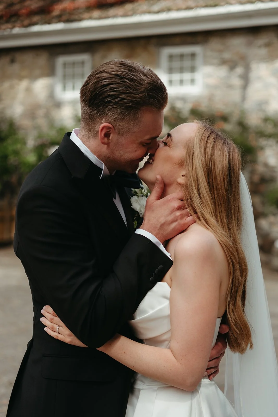 Et lykkelig par på bryllupsdagen, står tett sammen og smiler mens de kysser. Mannen har på seg en tuxedo, og kvinnen har på seg en hvit bryllupskjole.