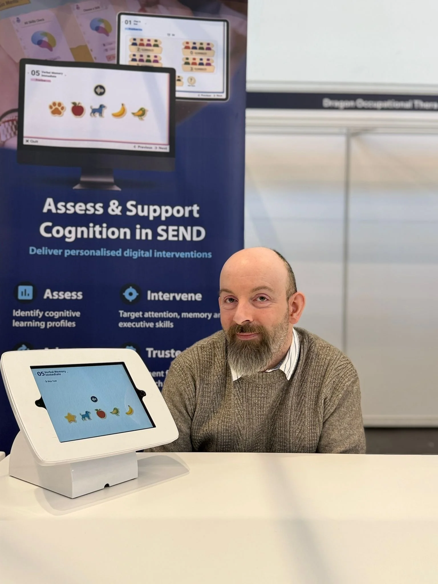 A man in graduation robes and cap smiling outdoors with trees and a body of water in the background.