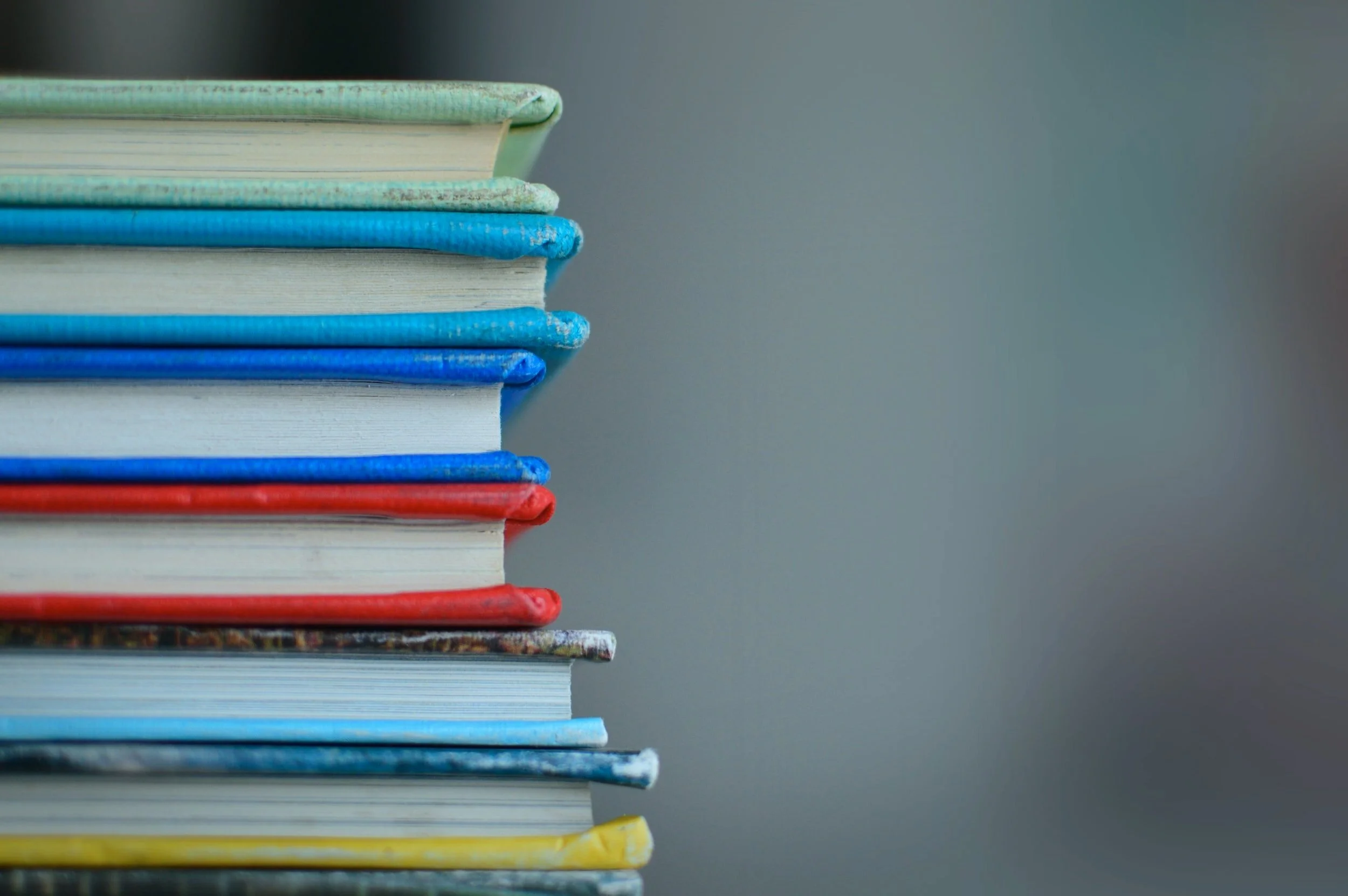 Stack of colorful books with a plain gray background.