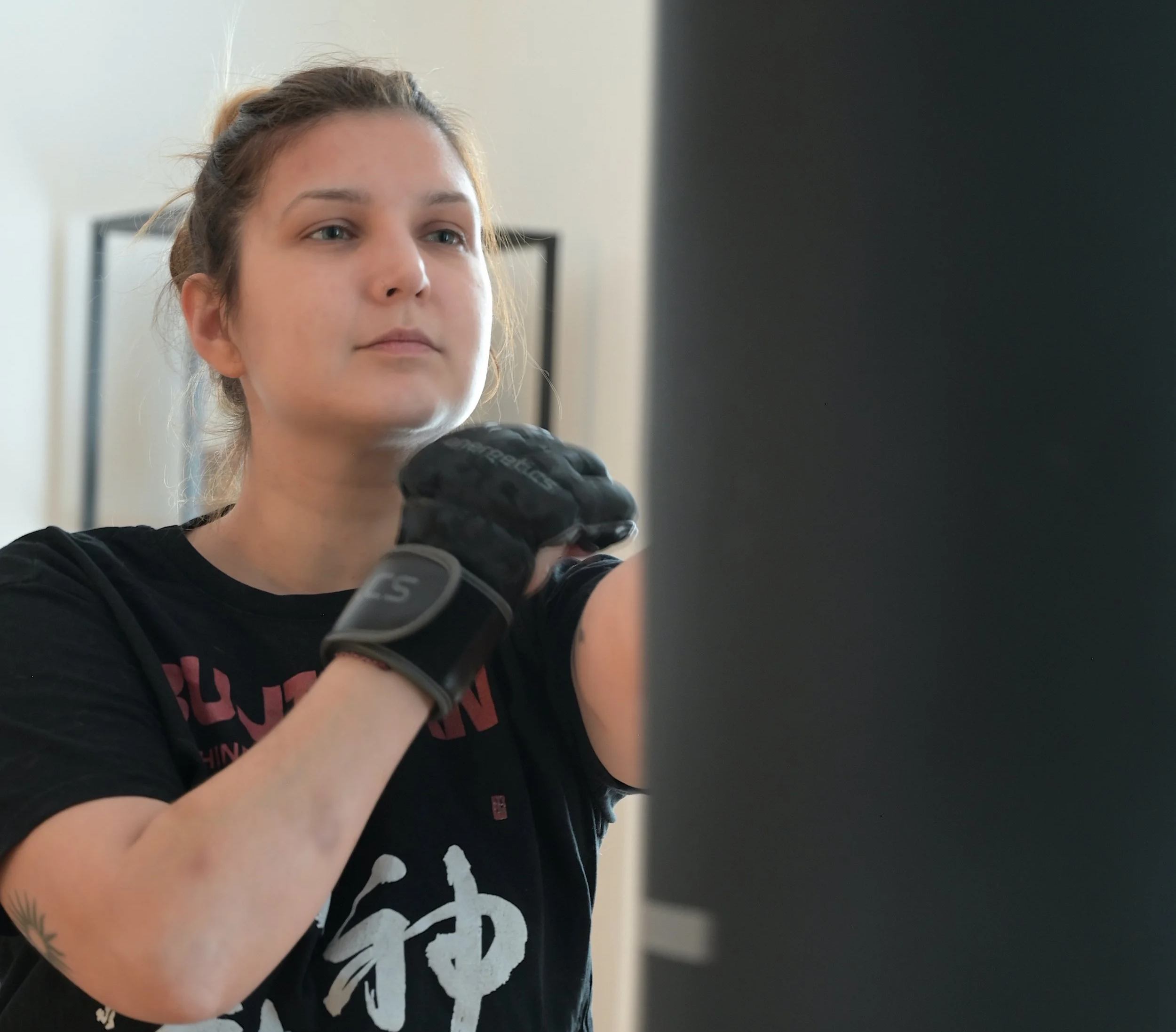 Junge Frau beim Kampfsporttraining, trägt schwarze Boxhandschuhe und T-Shirt, konzentriert sich auf ihren Schlag und ihre Atmung.