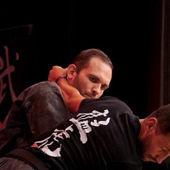Zwei Männer beim Kampfsport; einer schaut konzentriert, der andere ist nur teilweise sichtbar.