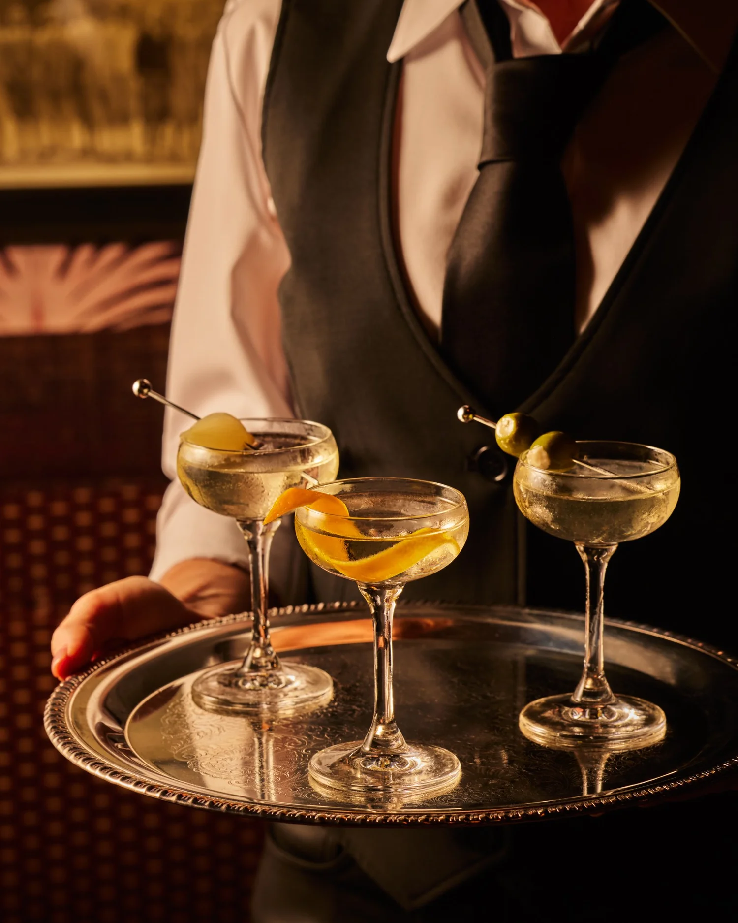 A server carrying three finished cocktails on a tray