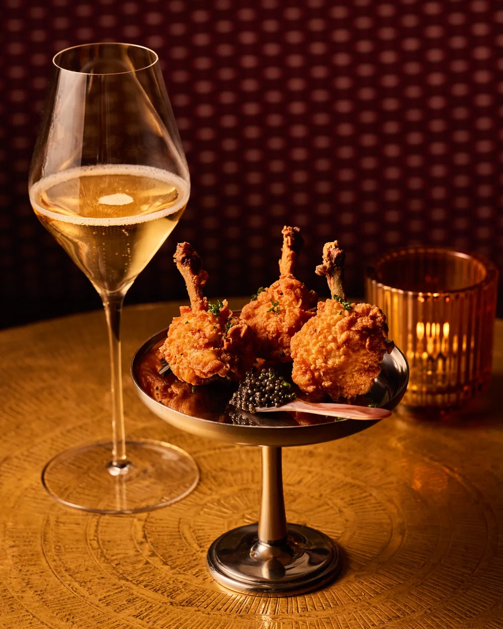 Fried chicken beside a glass of Champagne on a golden table