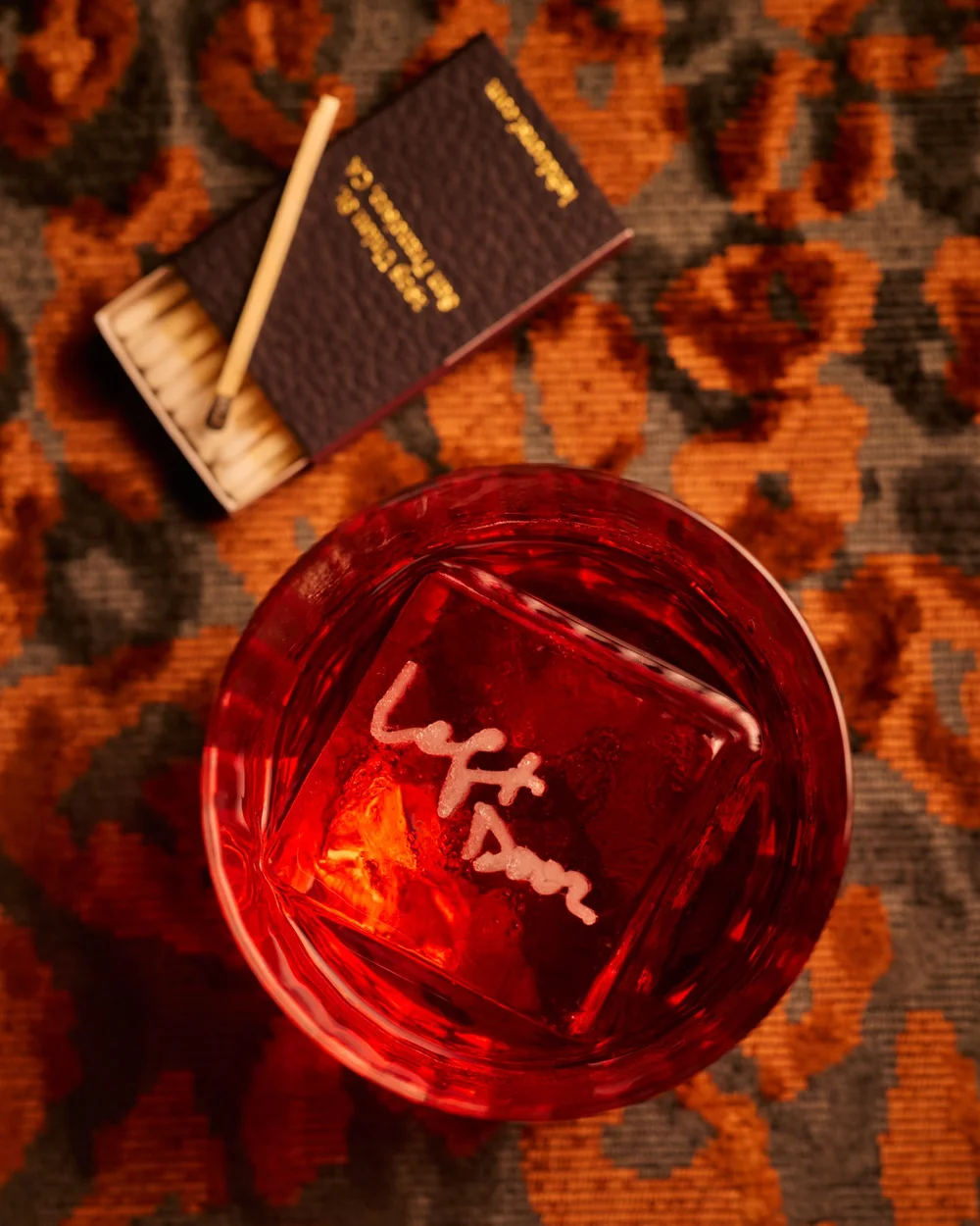 A Negroni with a Left Door-branded ice cube beside a matchbook
