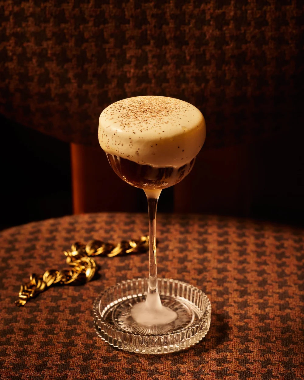 A cocktail resting on a chair beside a gold bracelet