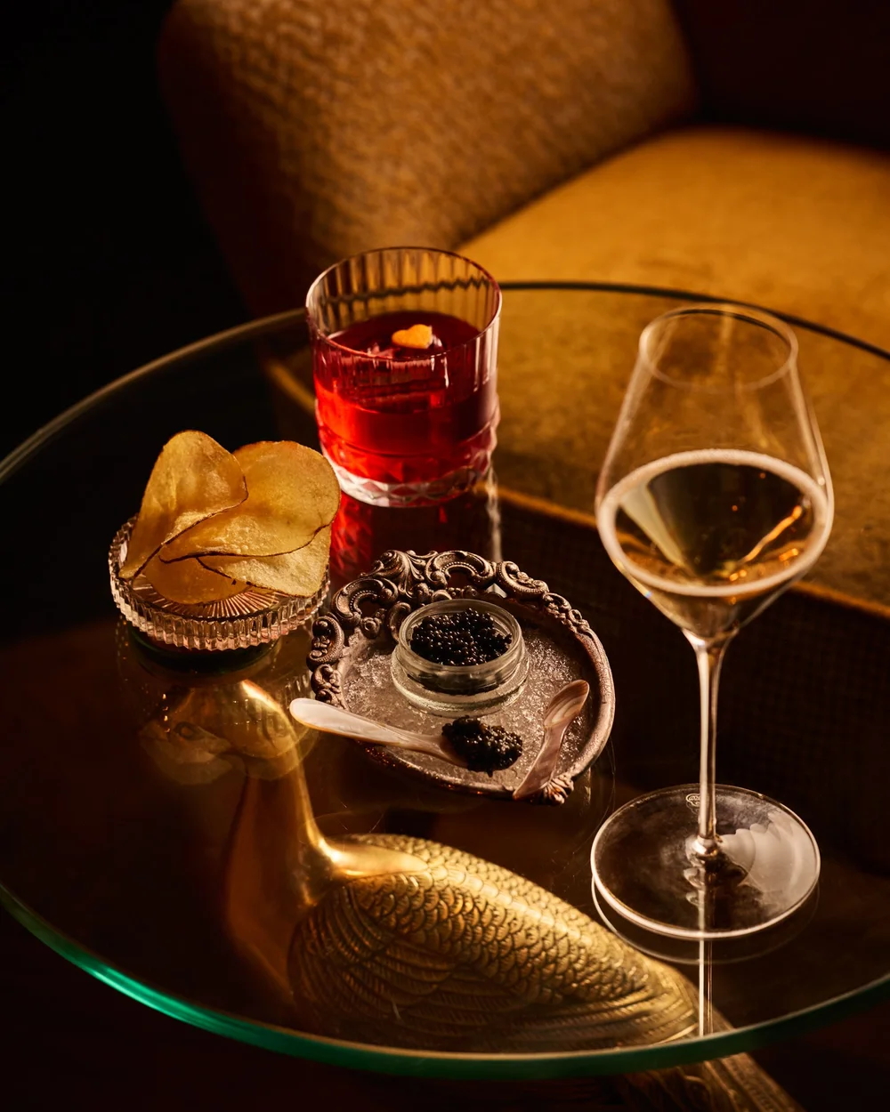 Chips, Champagne, caviar, and a cocktail arranged on a glass plate