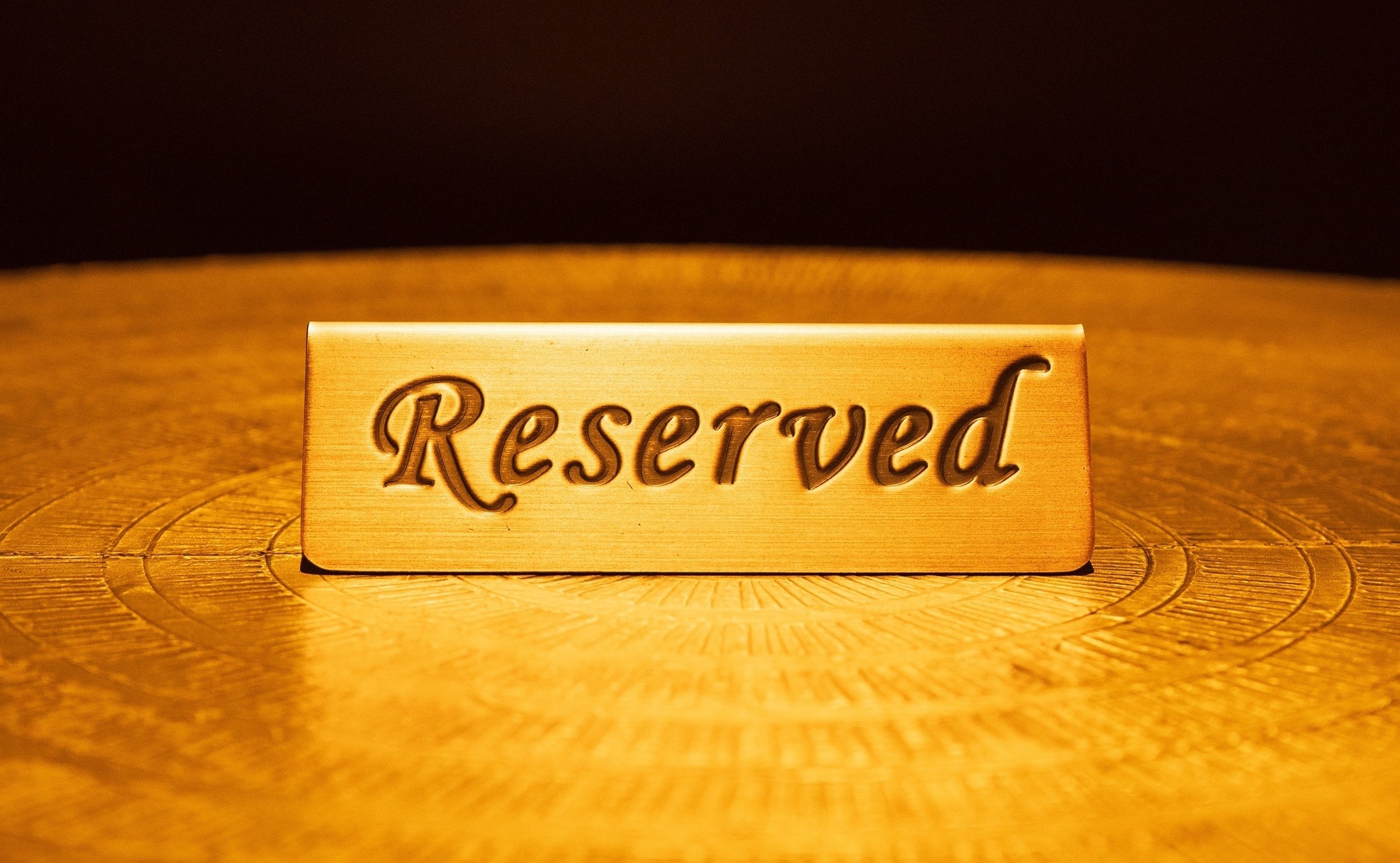 Brass reserved sign on golden table in front of dark background. Photo credit: Left Door