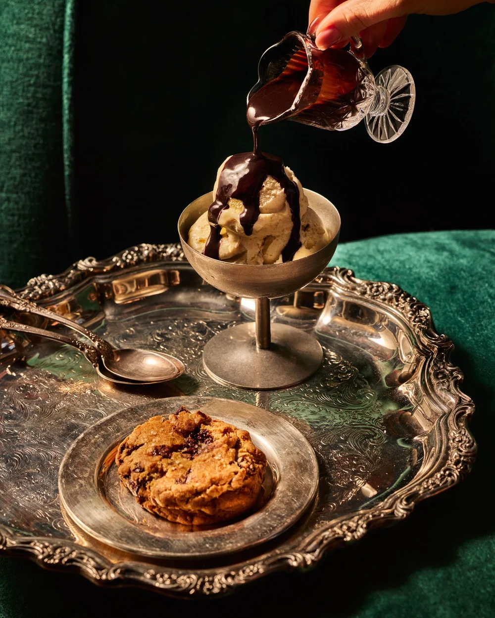 Chocolate sauce being poured over vanilla ice cream beside a cookie