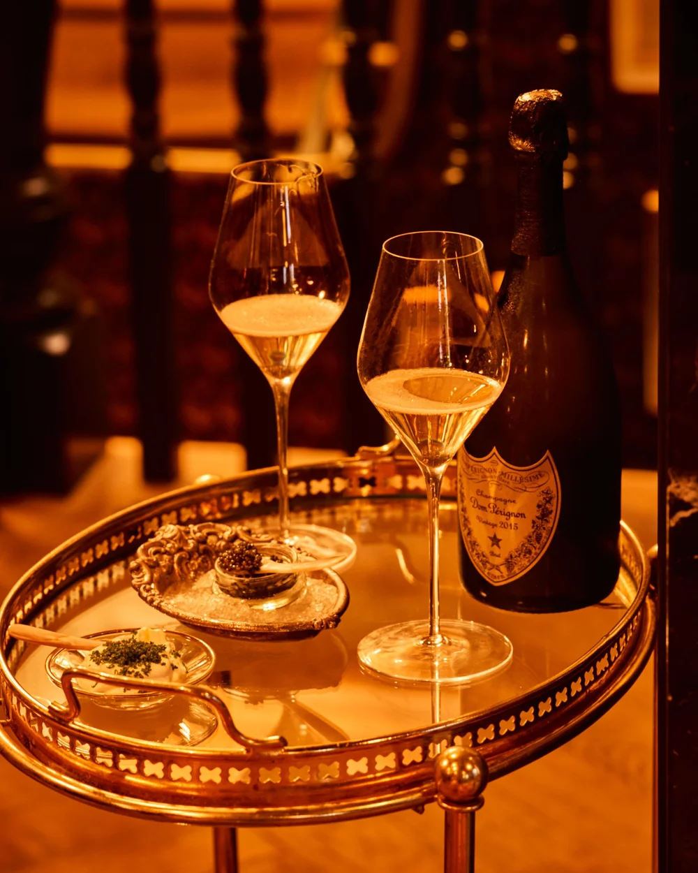 A bottle of Champagne with two glasses and caviar on a glass table