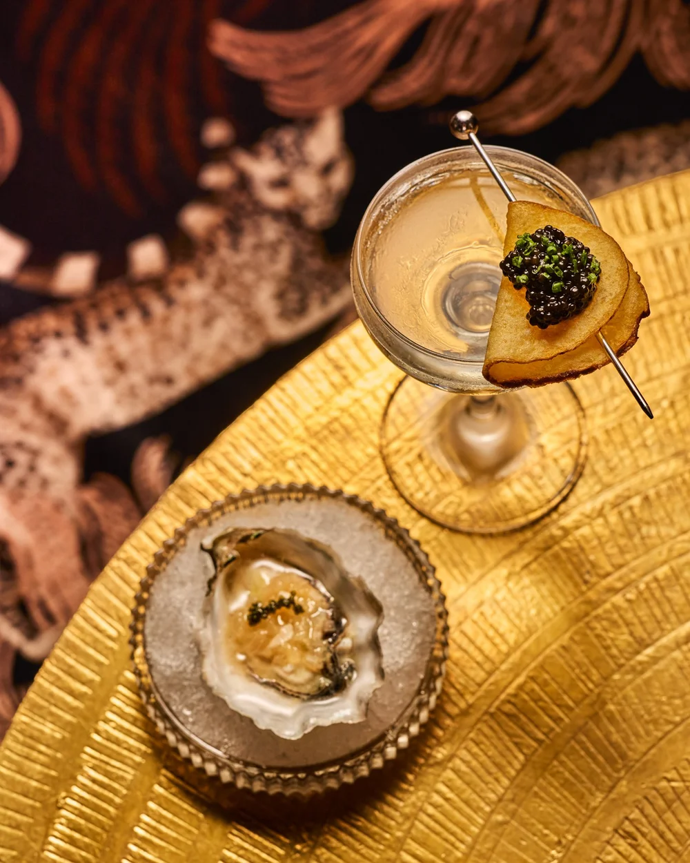 A martini with two olives beside a freshly shucked oyster