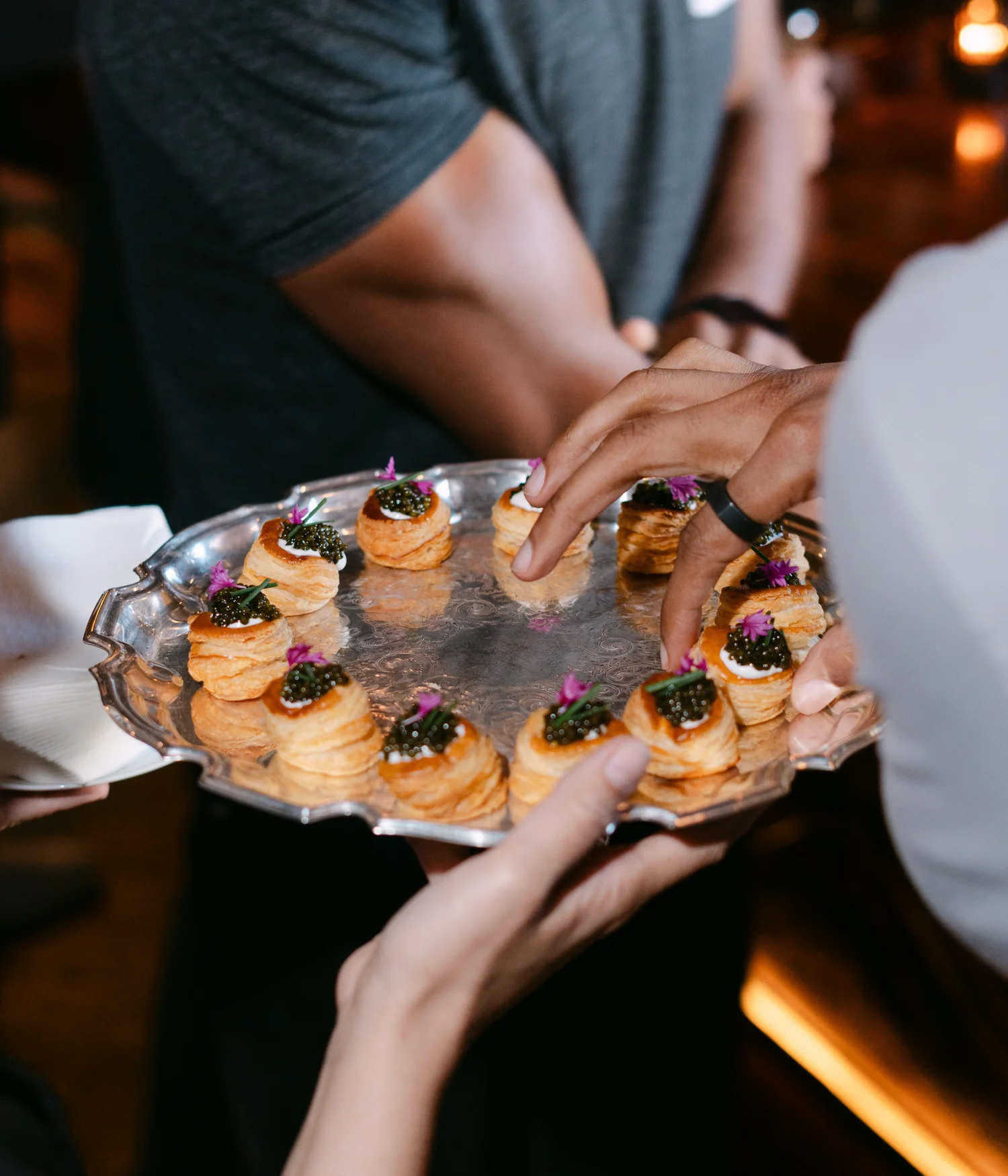 Guests selecting caviar-topped bites from a silver tray