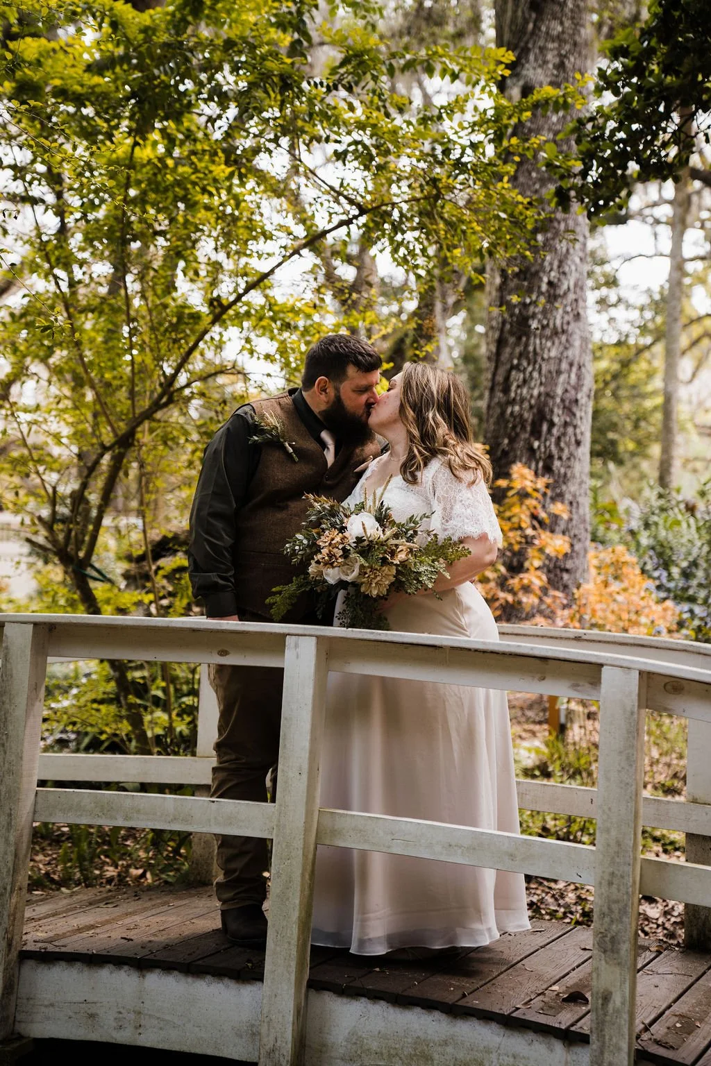 A bride and groom kissing on wood bridge in a forest