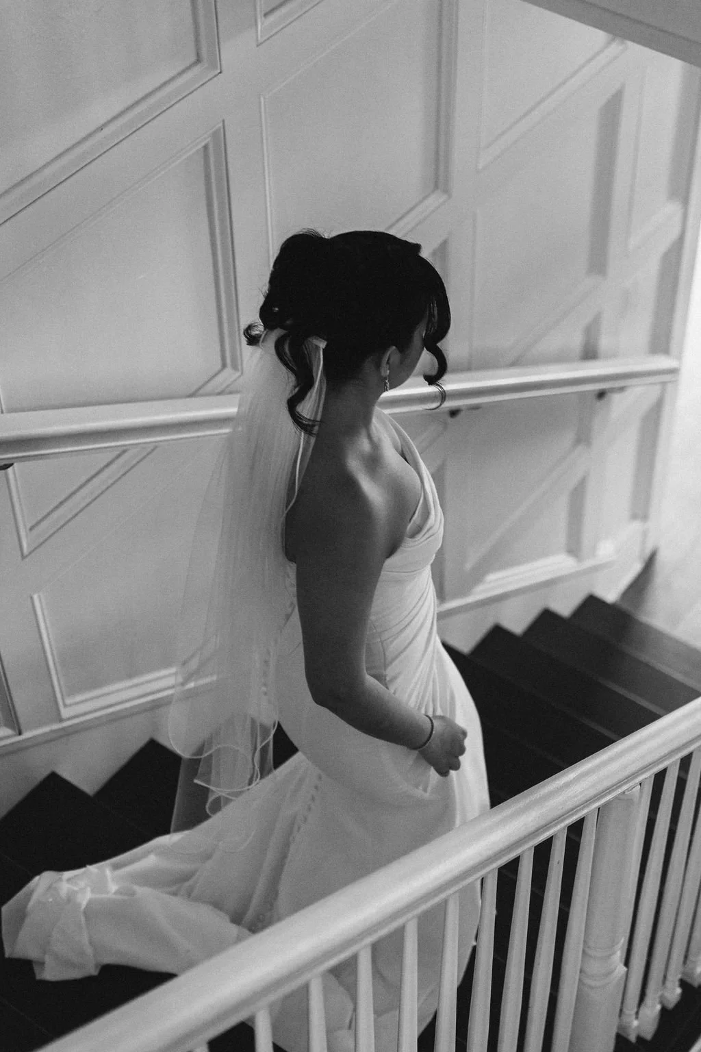 A woman in white dress walks down a white staircase with black carpet