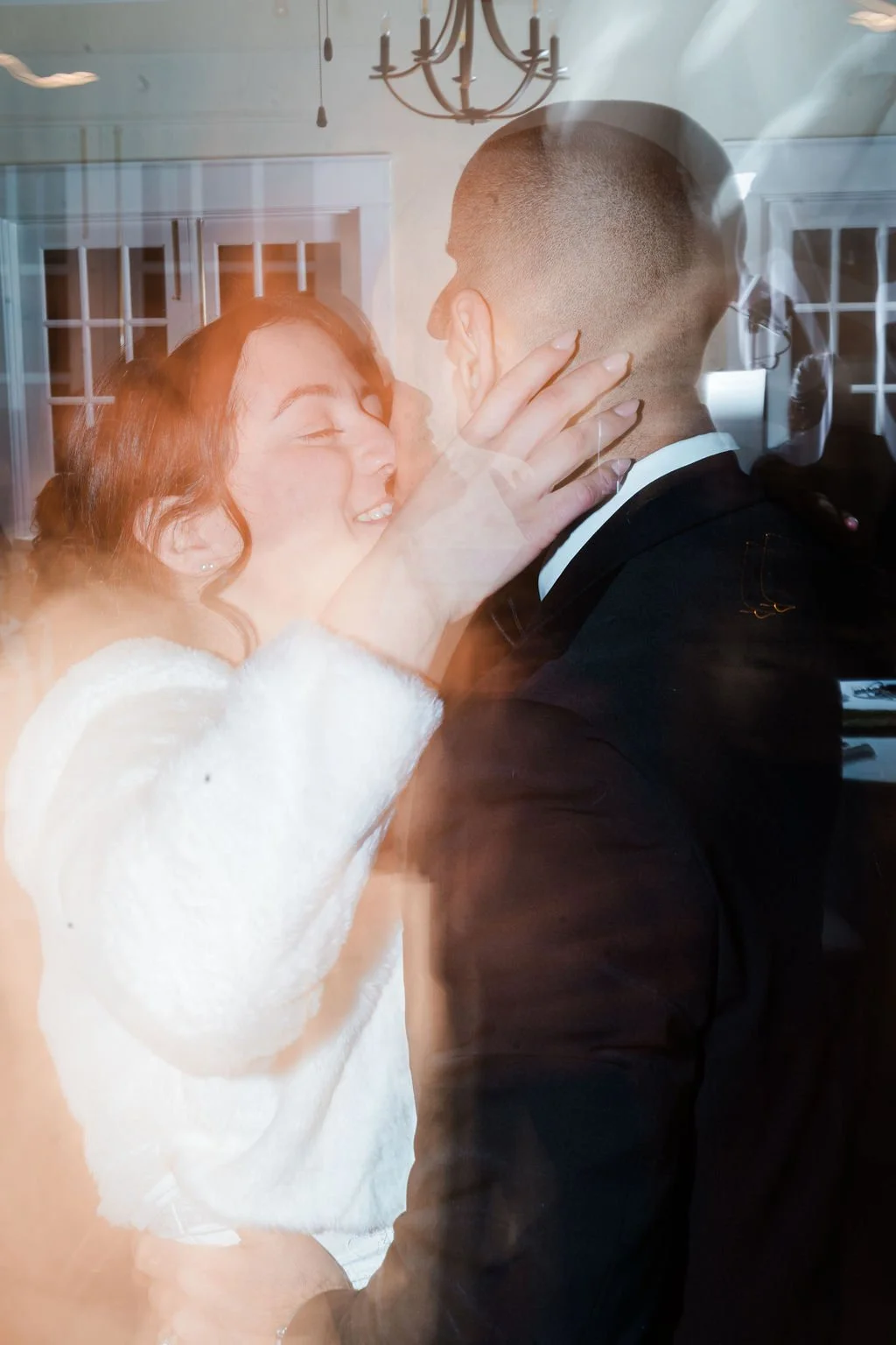 A blurry image of a woman in white fur coat touching the face of a man in black suit