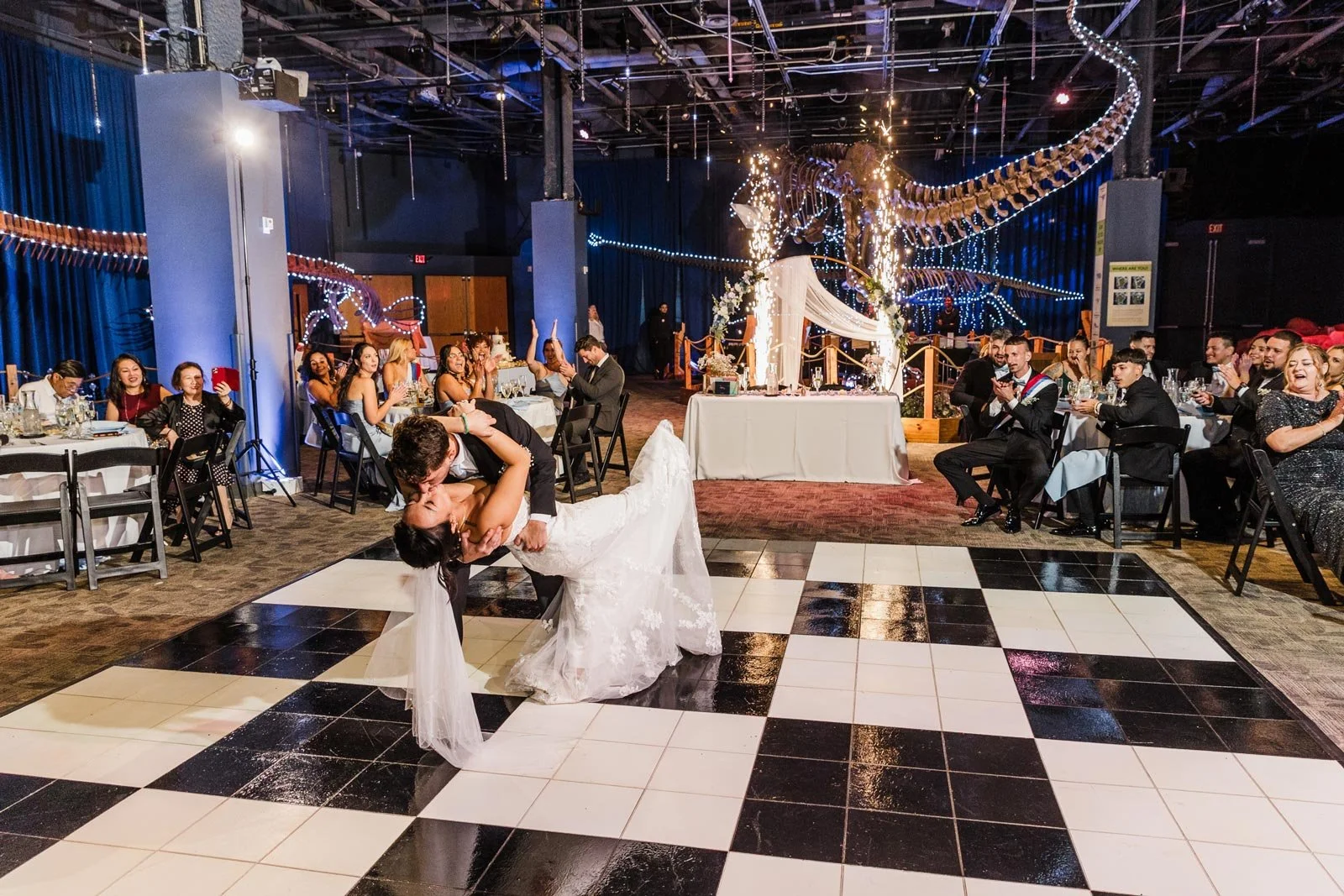 Bride and groom exchange a kiss during dance on black and white checkered dance floor at indoor wedding reception